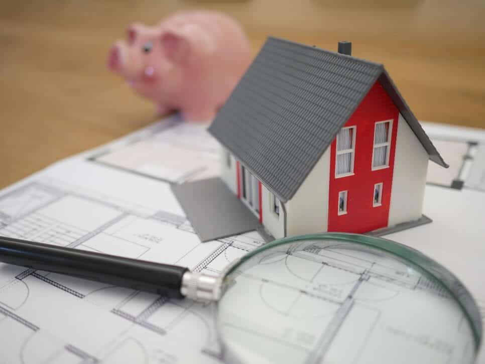 A model home, alongside a magnifying glass and a piggy bank