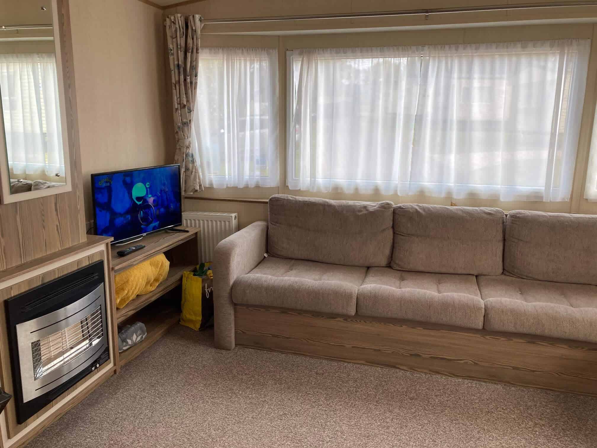 Bronze Caravan at Golden Sands Dawlish living room with brown sofa, large window, fireplace, mirror and TV.