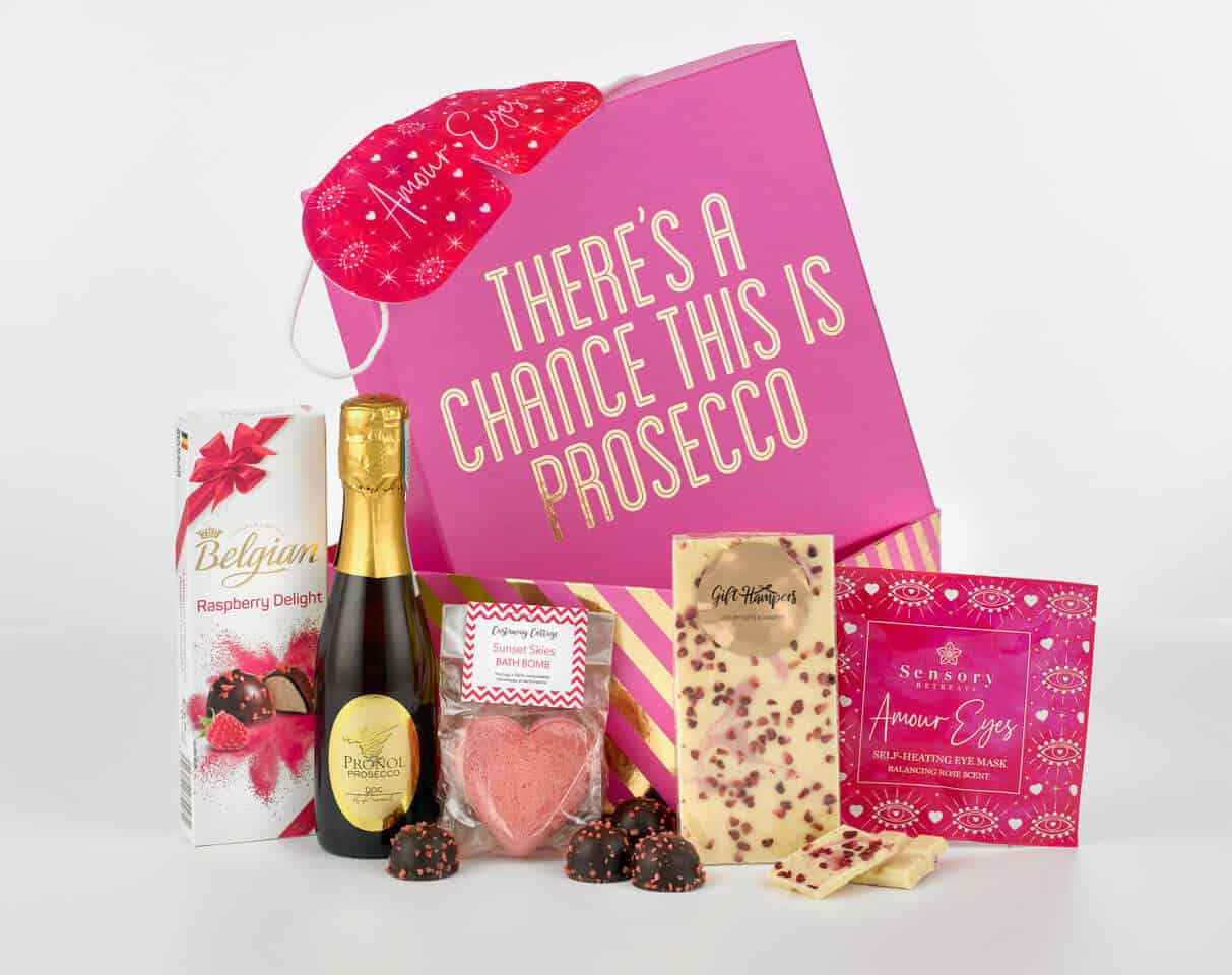 Pink hamper box with the contents of prosecco, a bath bomb, chocolates and a facemask around it.