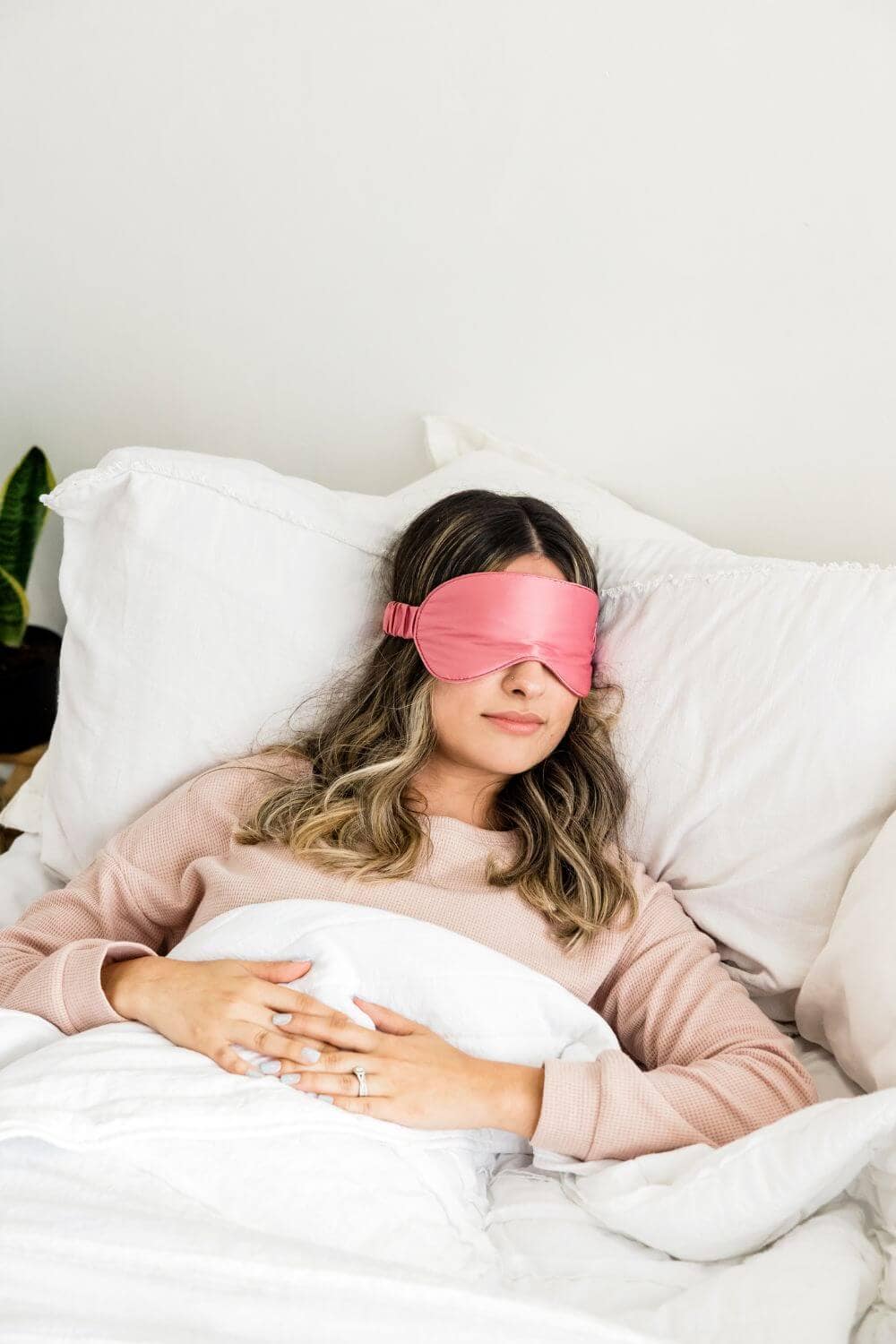A woman lying in bed wearing a pink sleep mask